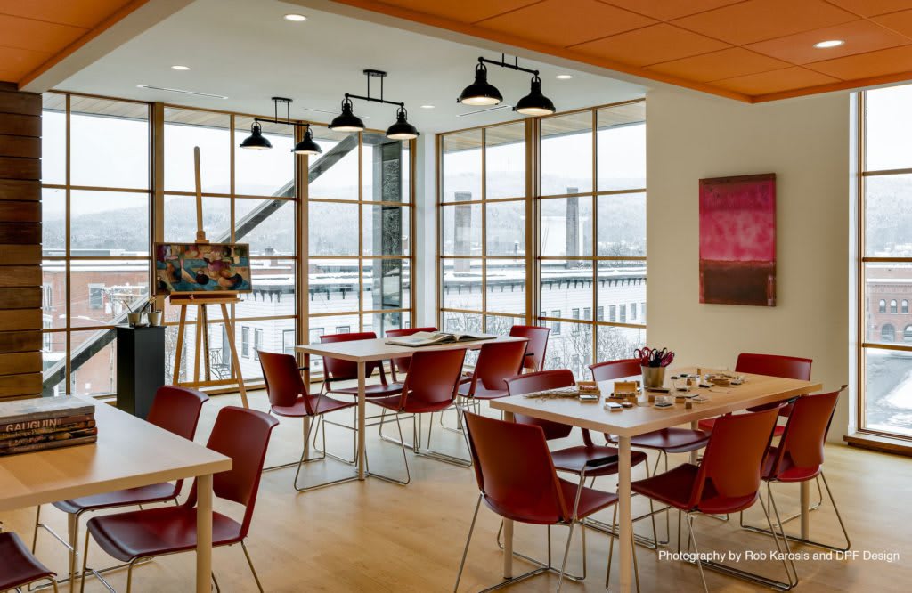 A modern dining area with large windows, featuring tables set for guests and artwork on display.