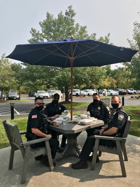 Four police officers seated at a patio table under an umbrella, wearing masks.