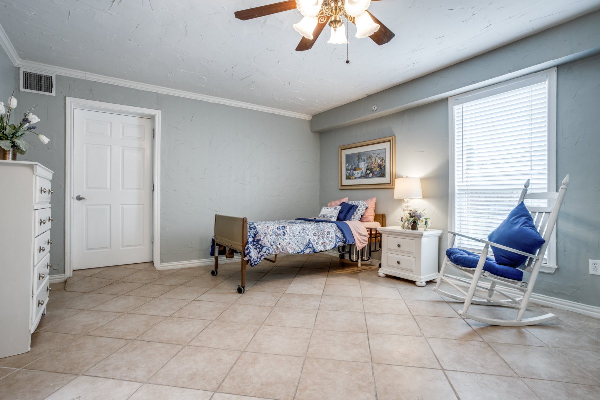 A minimalist bedroom with a single bed, ceiling fan, and tile flooring.