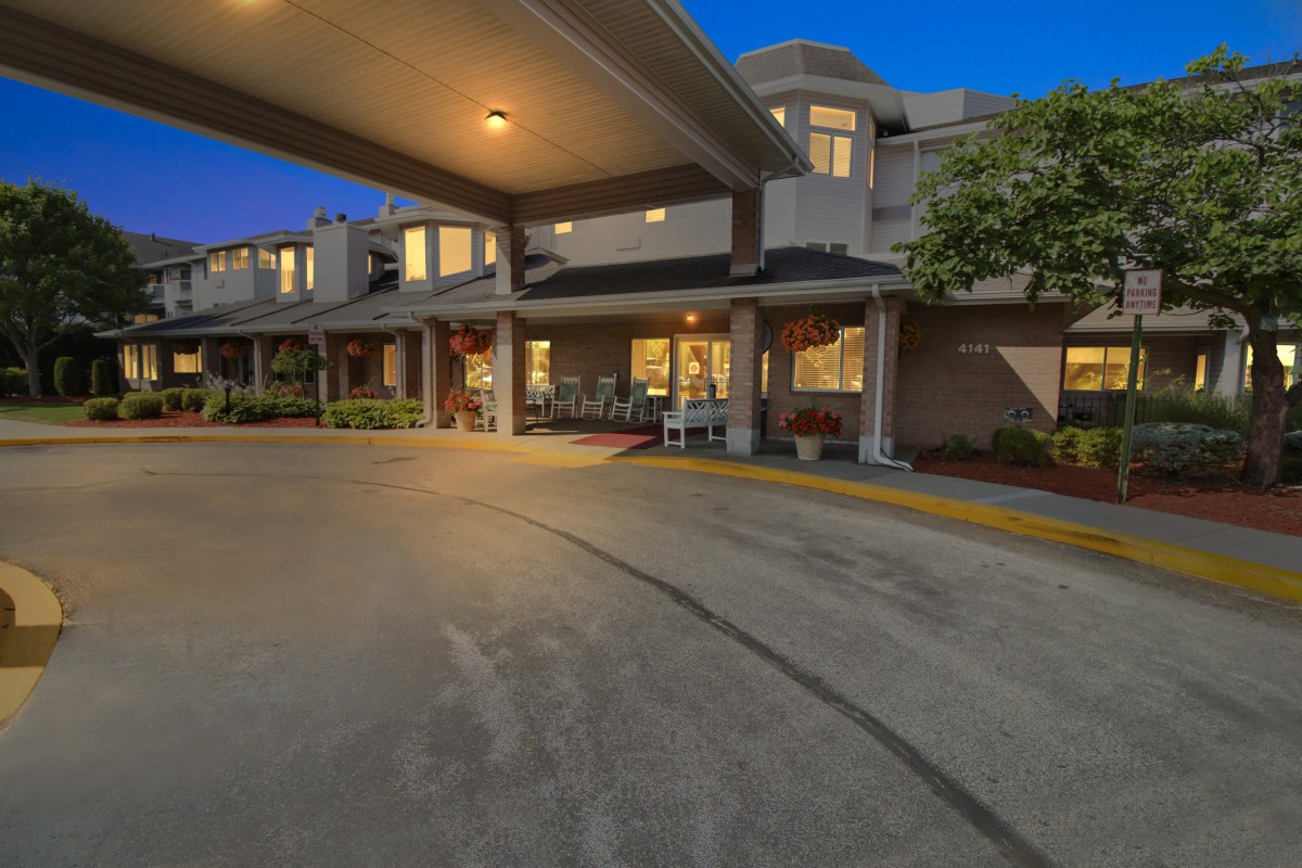 A well-lit building entrance with a covered driveway in the evening.