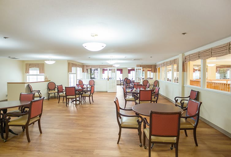 A bright and spacious dining area with wooden floors, furnished with multiple tables and chairs.