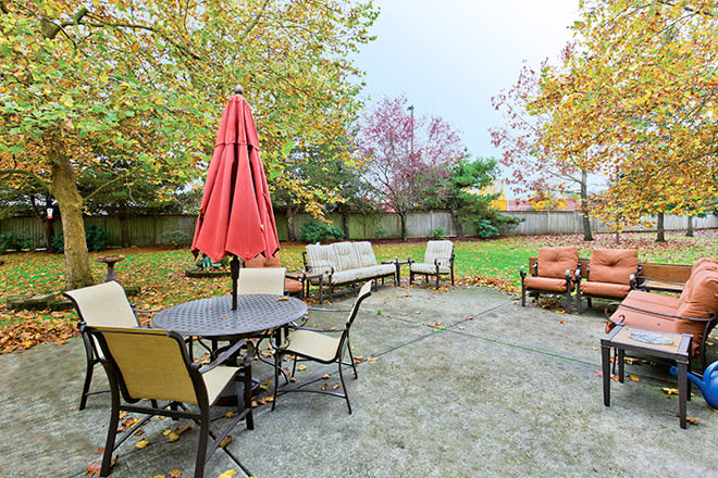 A cozy patio area with outdoor furniture, featuring a table with an umbrella and chairs, surrounded by trees with autumn foliage.