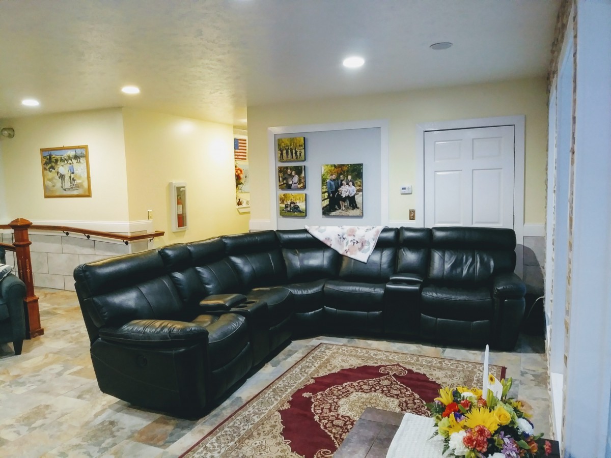 A cozy living room featuring a black leather sectional sofa, colorful rug, and decorative wall art.