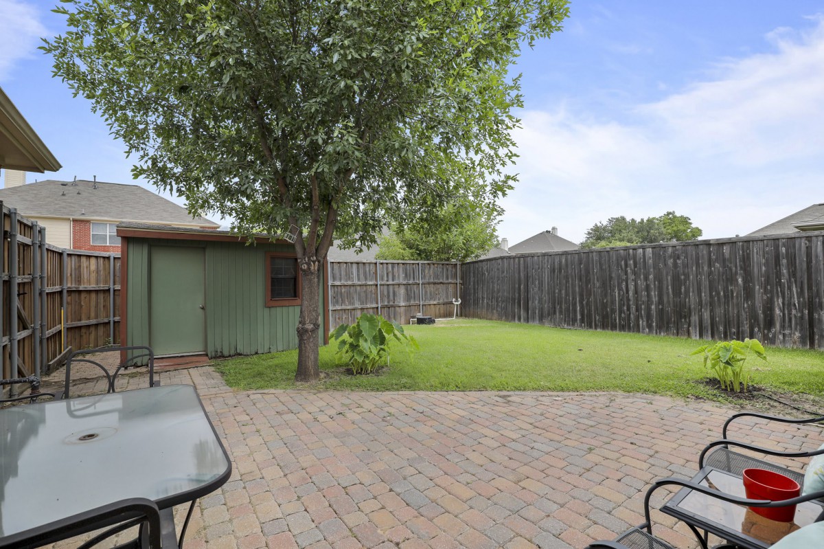 A peaceful backyard with a tree and a patio set on a sunny day.