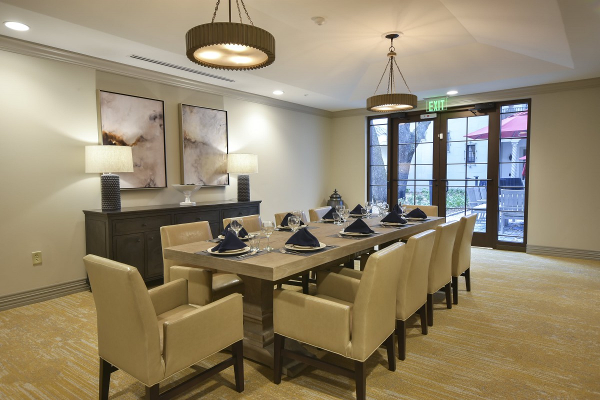 A modern, elegantly designed dining room with a large table and upholstered chairs, featuring contemporary lighting and artwork.