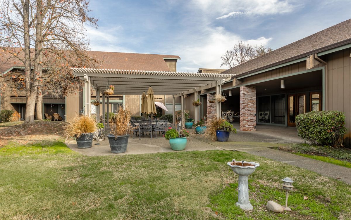 Cozy backyard patio featuring a pergola, outdoor seating, and a well-maintained garden with potted plants.
