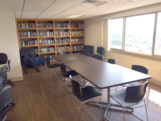 A conference room with a long meeting table surrounded by chairs and bookshelves along the wall.