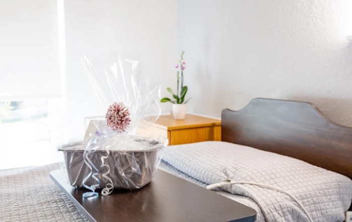 A cozy bedroom featuring a neatly wrapped gift basket on a table and an orchid plant on the bedside cabinet.