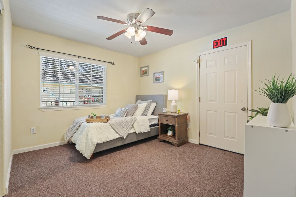 A cozy bedroom featuring a neatly made bed, ceiling fan, and a warm lamp on the nightstand.