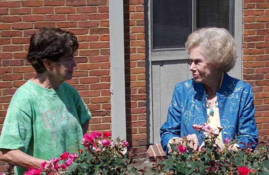 Two women having a conversation on a balcony with flowers.