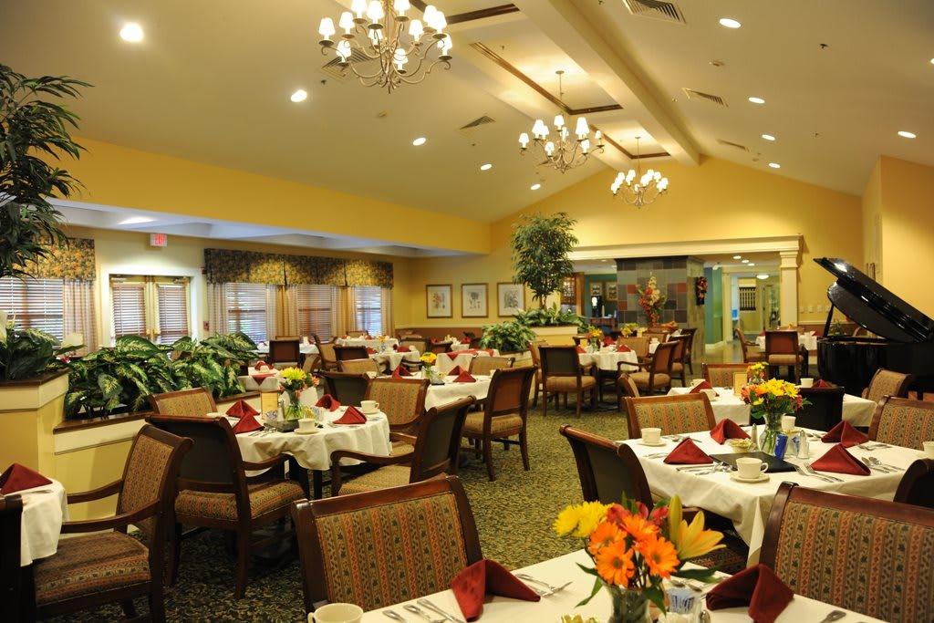 A beautifully decorated restaurant dining room with neatly arranged tables and chairs, adorned with floral centerpieces and elegant lighting.
