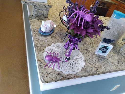 A whimsical purple-themed kitchen centerpiece featuring decorative spiders and flowers.