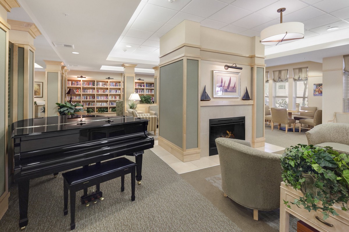 A cozy living room with a grand piano, fireplace, and extensive bookshelves.