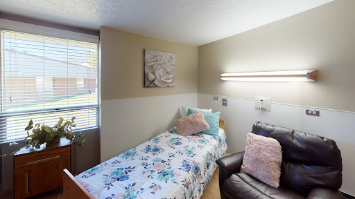 A cozy bedroom featuring a single bed with floral bedding, a comfortable chair, and soft lighting.