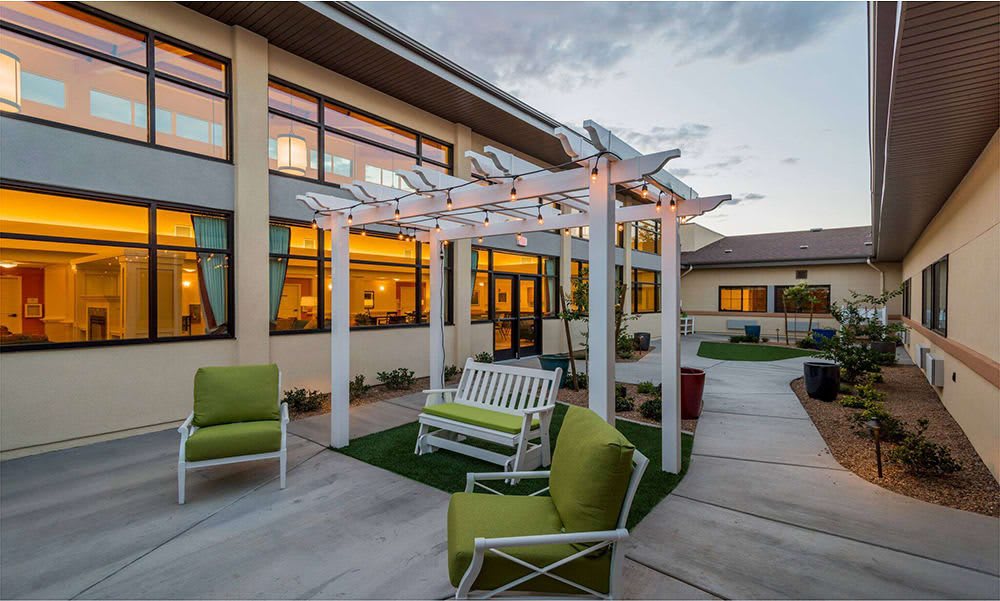 A cozy outdoor patio area with a pergola, swing, and green cushioned chairs at dusk.