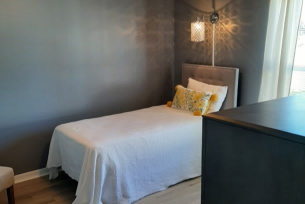 A modern minimalist bedroom featuring a single bed with gray walls and stylish lighting.