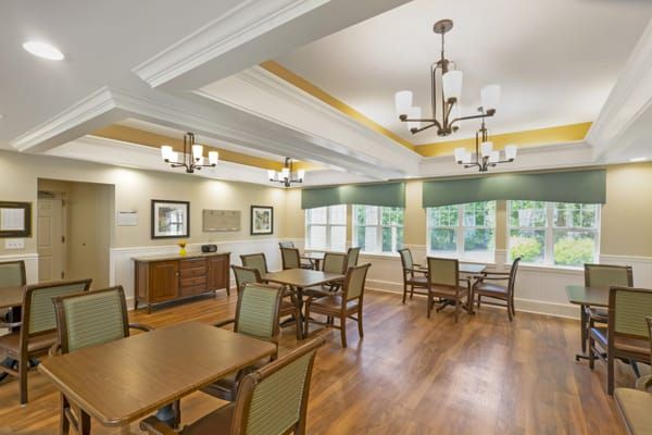 A well-lit dining room with wooden floors, tables and chairs, illuminated by chandeliers.