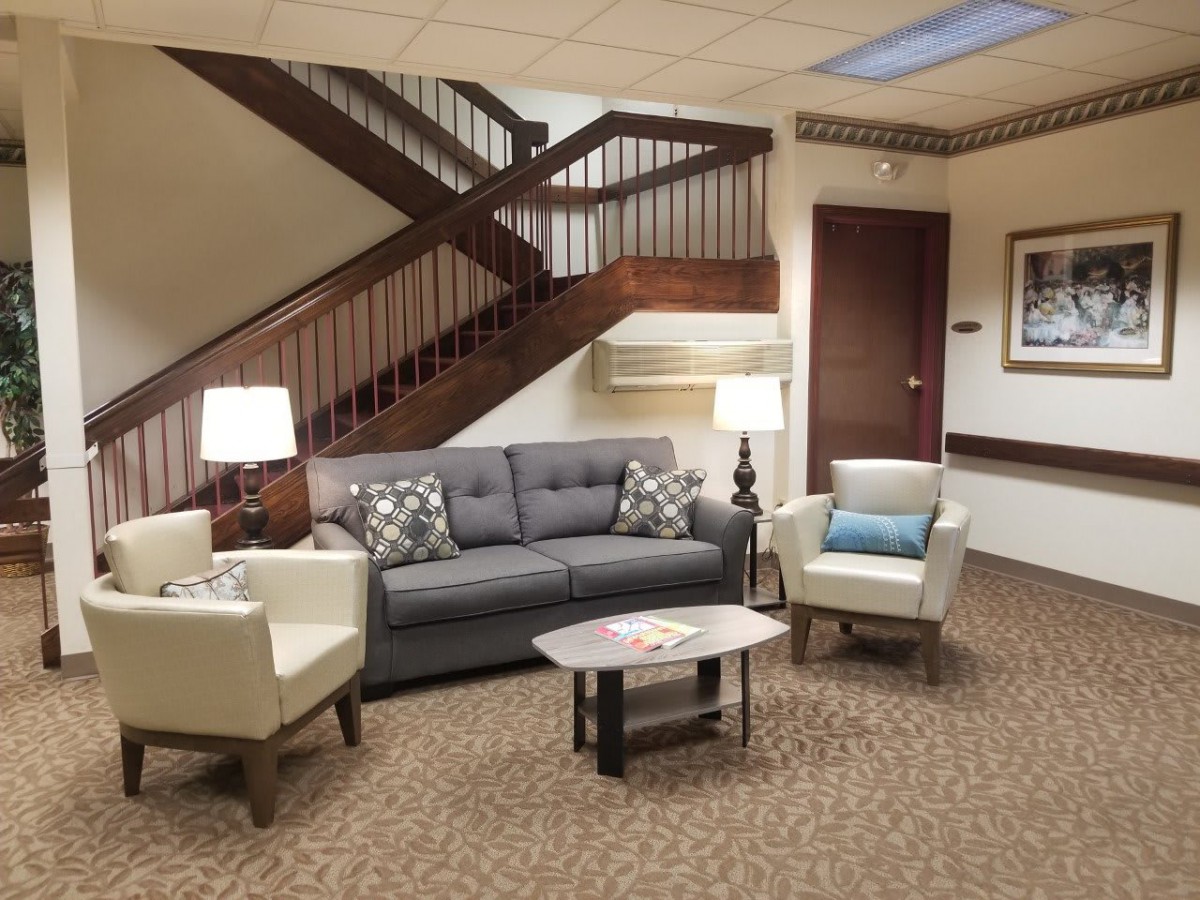 A comfortable lobby area featuring a sofa, two chairs, and a small coffee table with lamps under a staircase.