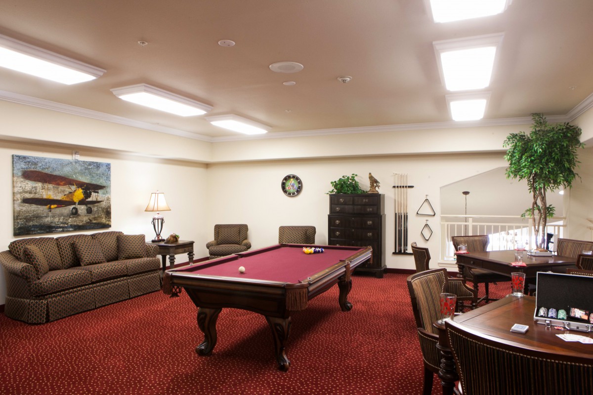 A cozy game room featuring a red pool table, comfortable seating, and warm lighting.