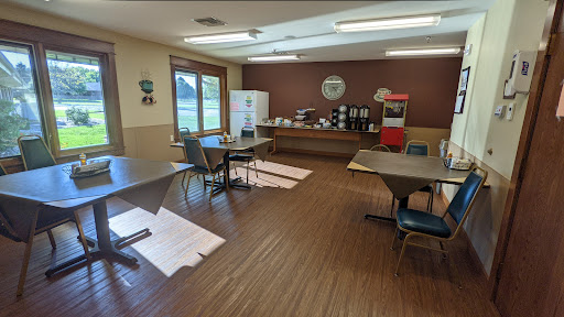 A cozy indoor space with tables and chairs, featuring a kitchenette area for refreshments.