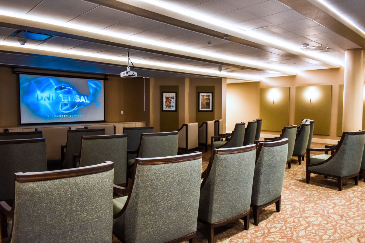 A small theater room with rows of comfortable chairs facing a projection screen.