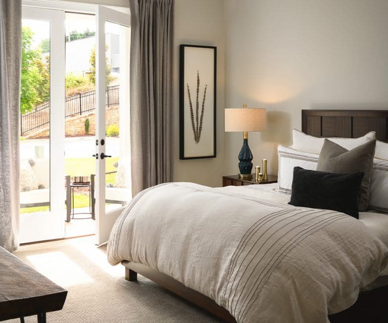 A cozy, well-lit bedroom with elegant decor and large windows overlooking a garden.
