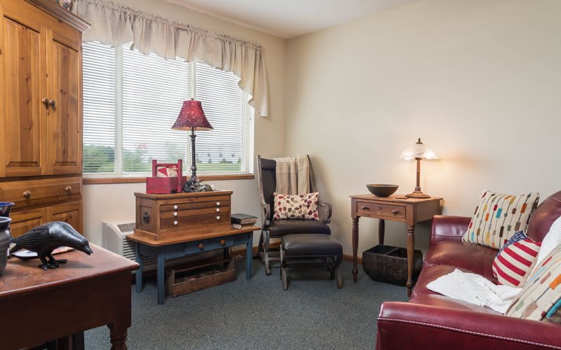A cozy living room with wooden furniture and lamps near a window.
