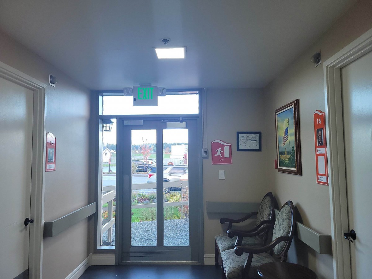 A small hallway with an exit door, chairs, and paintings on the wall.
