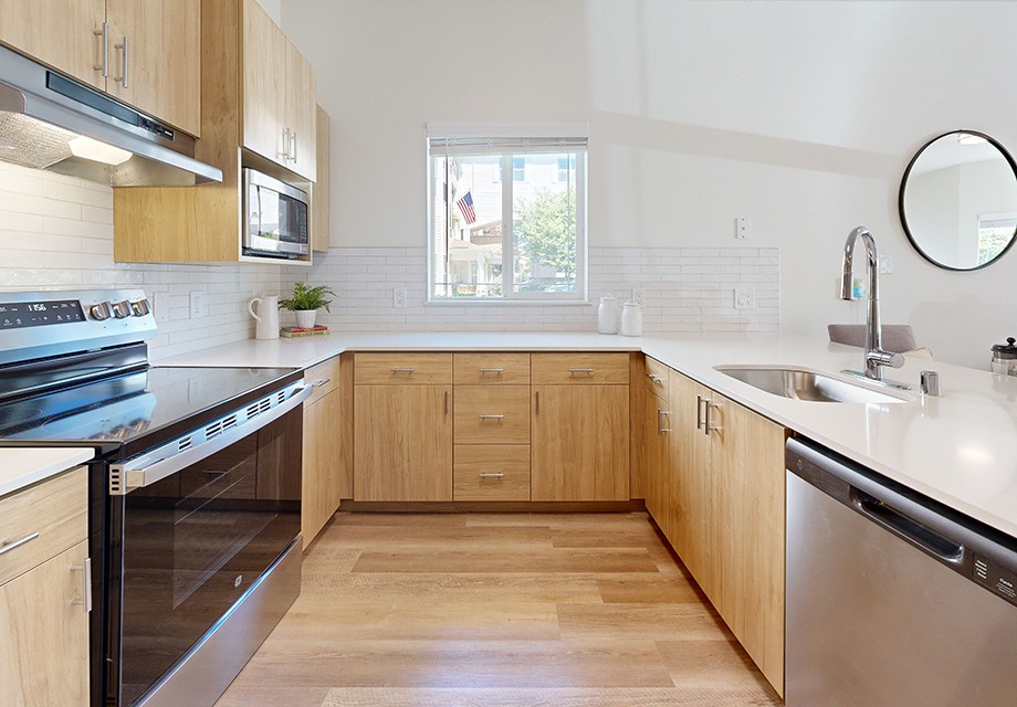 A modern kitchen with wooden cabinets, sleek appliances, and a bright window.