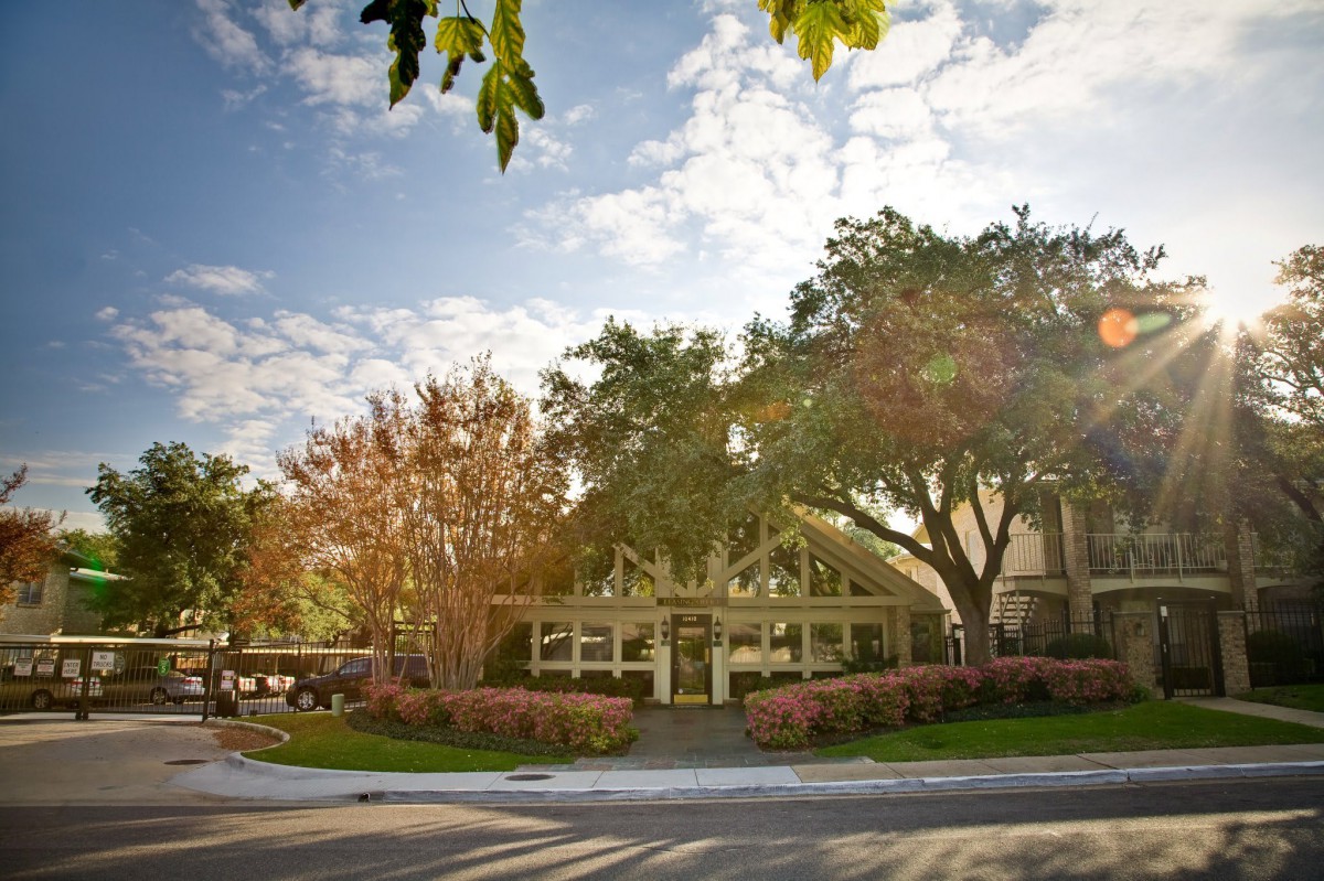 A peaceful street view of a building surrounded by trees under a partly cloudy sky.