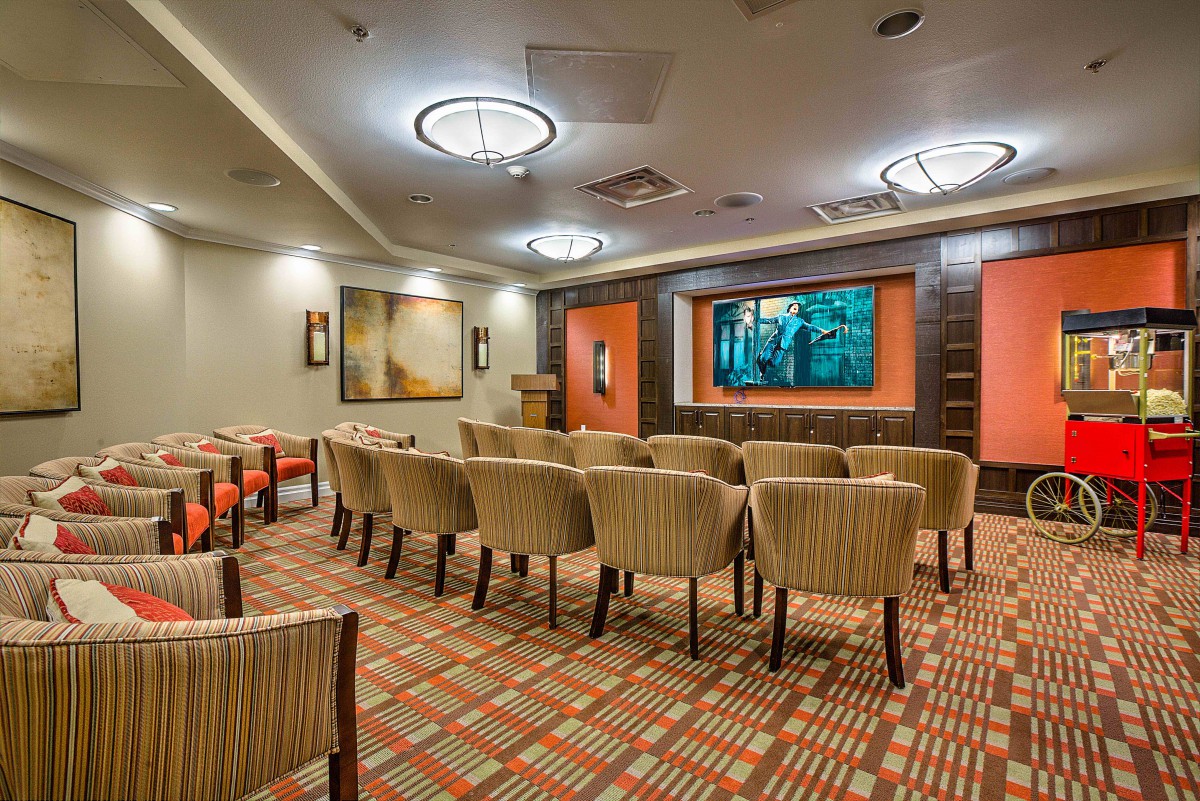 A well-lit conference room with rows of chairs facing a large screen at the front.