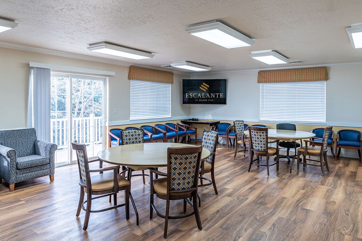 A modern dining area with wooden flooring, round tables, and chairs, featuring large windows and contemporary lighting.