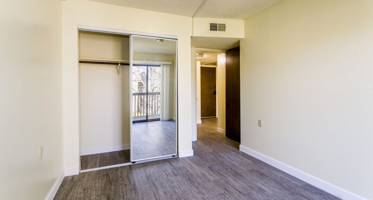 An empty room with a mirrored closet door, wood flooring, and a view of the balcony through the window.