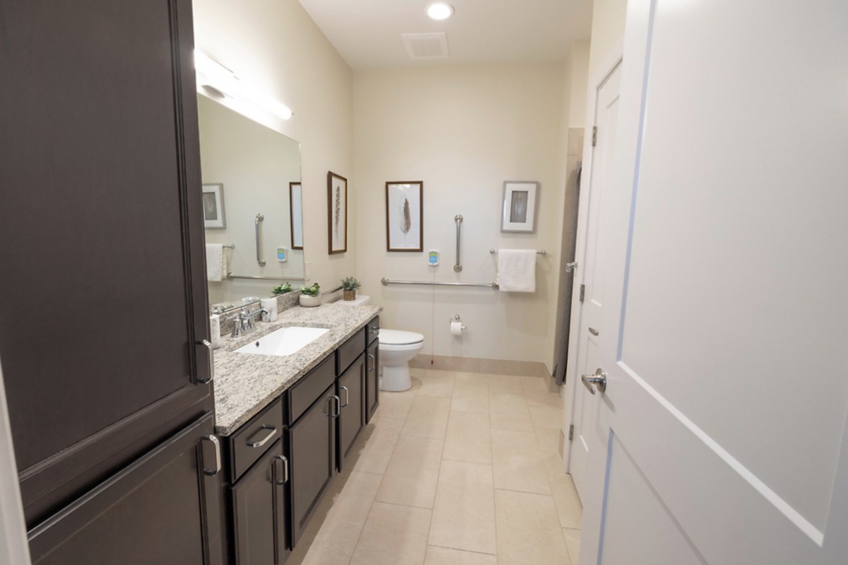 A modern bathroom with a sleek design featuring a large mirror, double sinks, and tiled flooring.