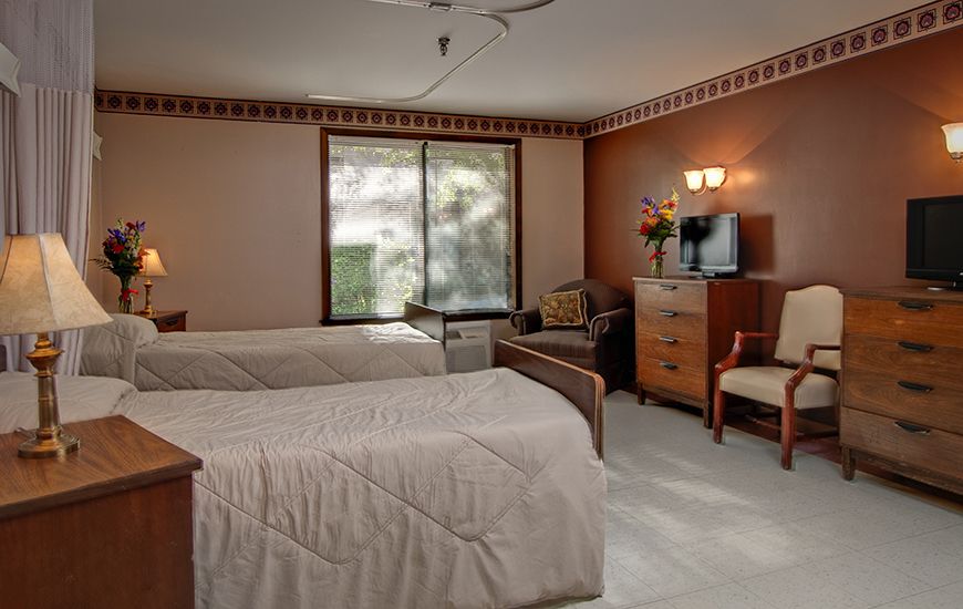 A cozy hotel room featuring two double beds, a TV cabinet, chairs, and soft lighting.