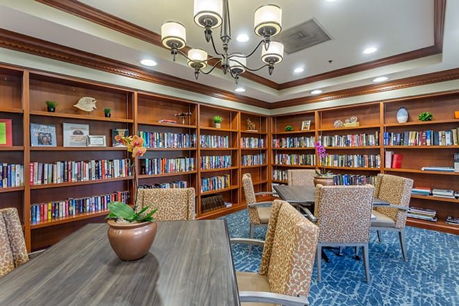 A cozy library room with wooden bookshelves, a table surrounded by chairs, and a chandelier overhead.