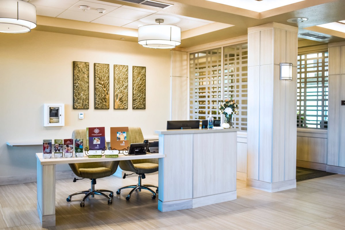 A modern office reception area with a front desk, chairs, and decorative art on the wall.