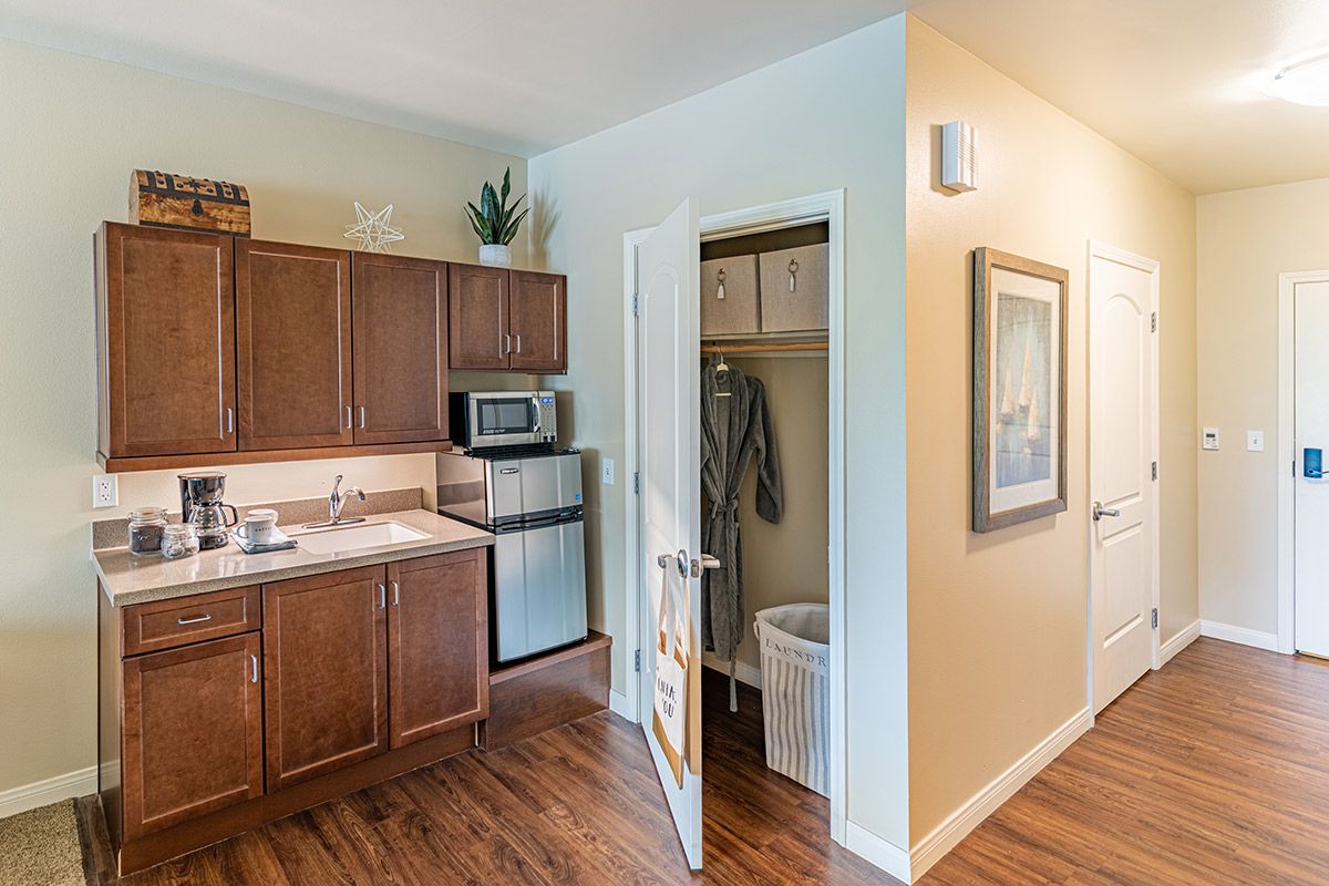 A cozy apartment kitchen with wooden cabinets, a microwave, and a small refrigerator next to an open closet door.