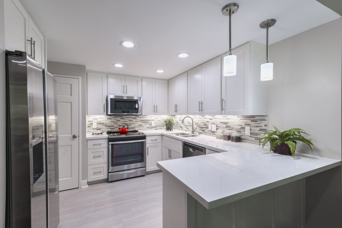 A modern kitchen with white cabinets, stainless steel appliances, and stylish lighting.