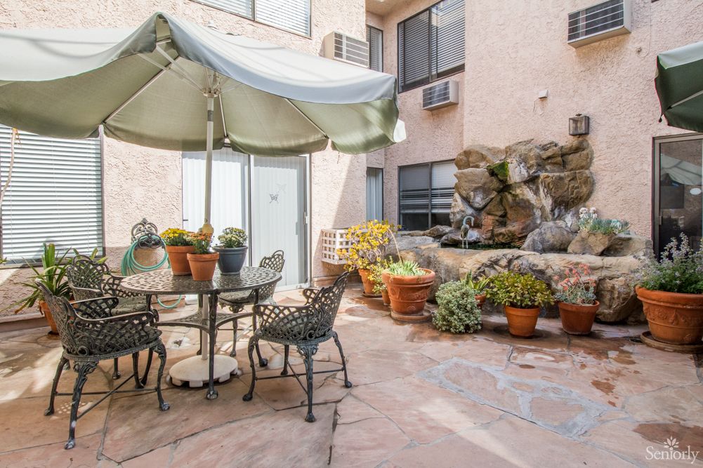 A cozy courtyard featuring a patio table with an umbrella, surrounded by potted plants and a decorative fountain.