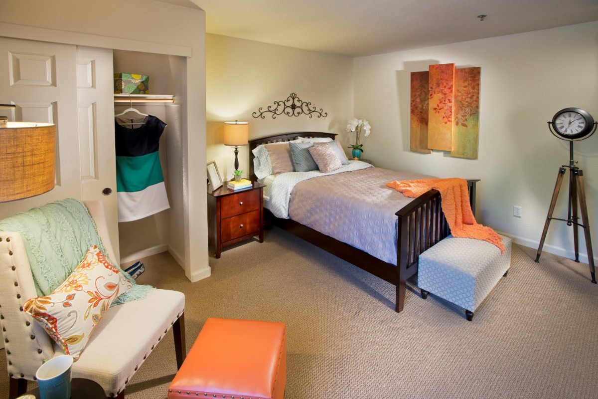 A cozy bedroom with warm decor, featuring a neatly made bed, a small closet, and a bedside lamp.
