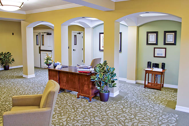 A welcoming office reception area with a desk, plants, and hallway in the background.