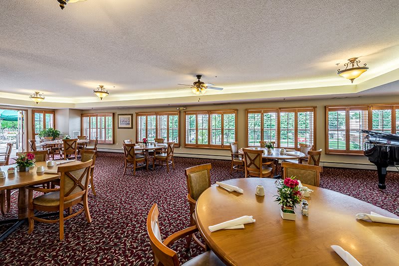 A spacious dining room with neatly arranged tables and chairs, featuring large windows and warm lighting.