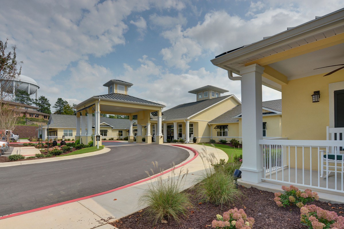 A modern building entrance with landscaped surroundings and a cloudy sky.