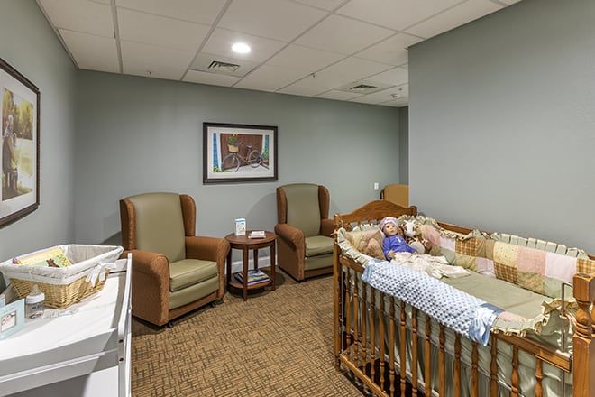 A cozy nursery room with a crib, two chairs, and decor.
