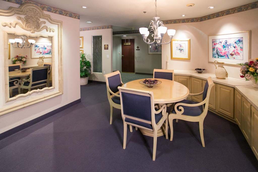 A cozy dining area with a round table, elegant chairs, and a chandelier above, surrounded by framed art and a large mirror.