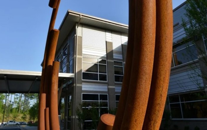 A modern building exterior viewed through a rusty metal sculpture.