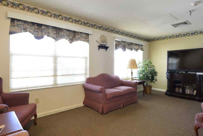 A cozy living room with a sofa, large windows, and decorative curtains.