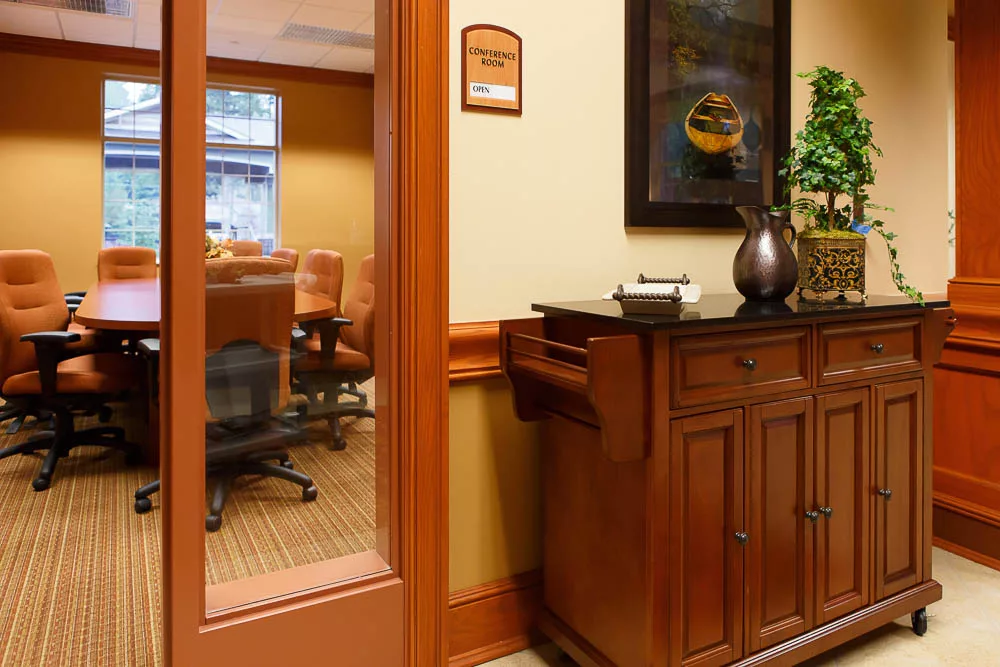 A view of a meeting room through a glass door, featuring a conference table and chairs, with a wooden cabinet in the foreground.