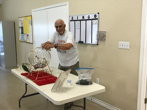 An elderly man prepares for a game of bingo, ready to draw numbers from the spinning cage.